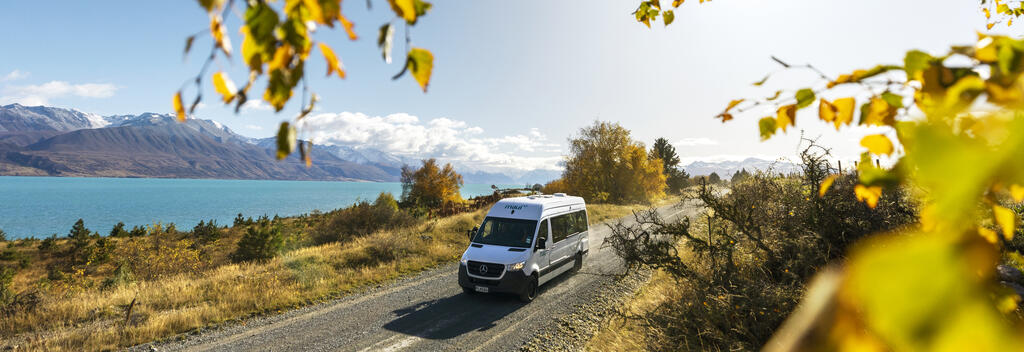 Campervan driving on a scenic road by blue Lake Pukaki with mountain backdrop