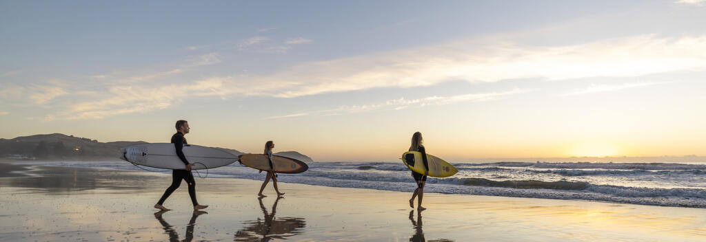 Surfers getting in the water at Wainui Beach at sunrise